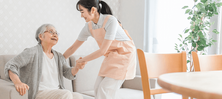 ソファから立ち上がる利用者様の手を取って介助する看護師