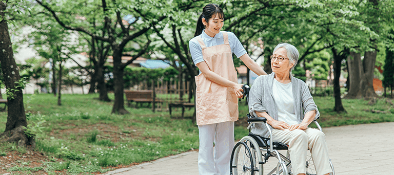 公園で車椅子の利用者様と散歩する看護師